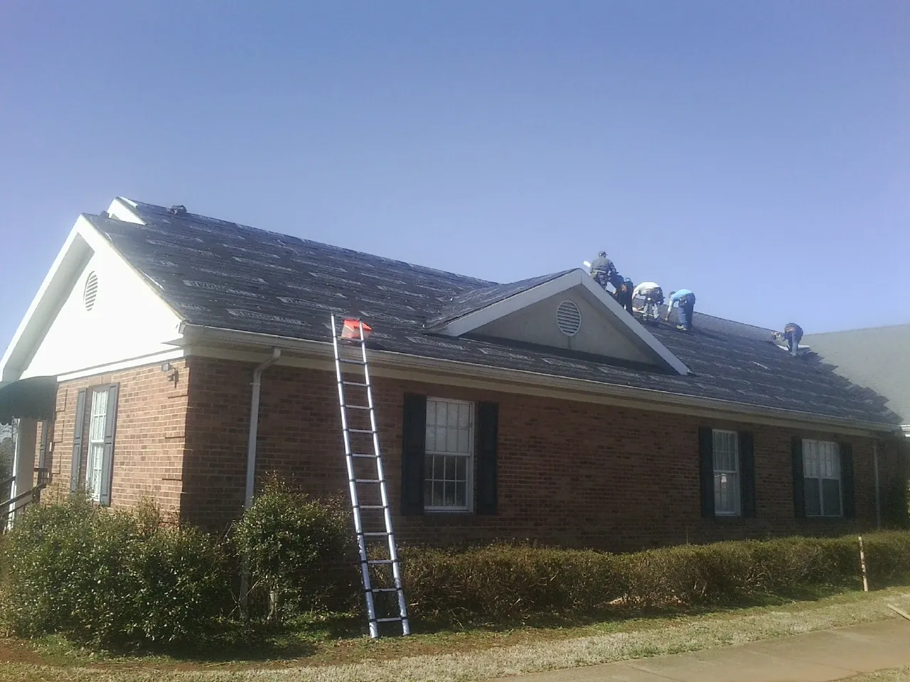 Crew tearing shingles off a brick ranch roof with a ladder set — Metal Roof Repair work by our crew in Dukedom