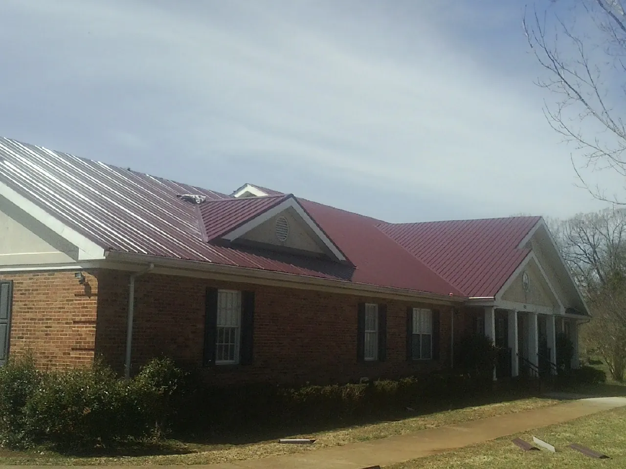 Red metal roof with gabled entries on a long brick building, from a Hail Damage Roof Repair job in Dukedom