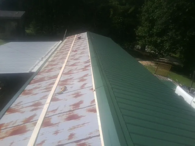 Old rusted panels beside newly installed green metal roofing — Wind Damage Roof Repair by Roofing Brothers in Dukedom