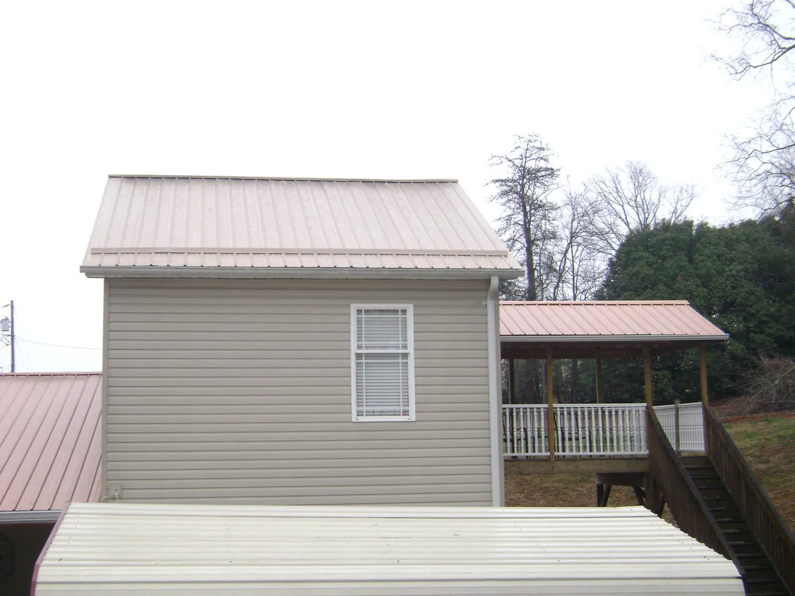 Tan metal roofs on a two story addition and attached porch, from a Roof Replacement job in Dukedom